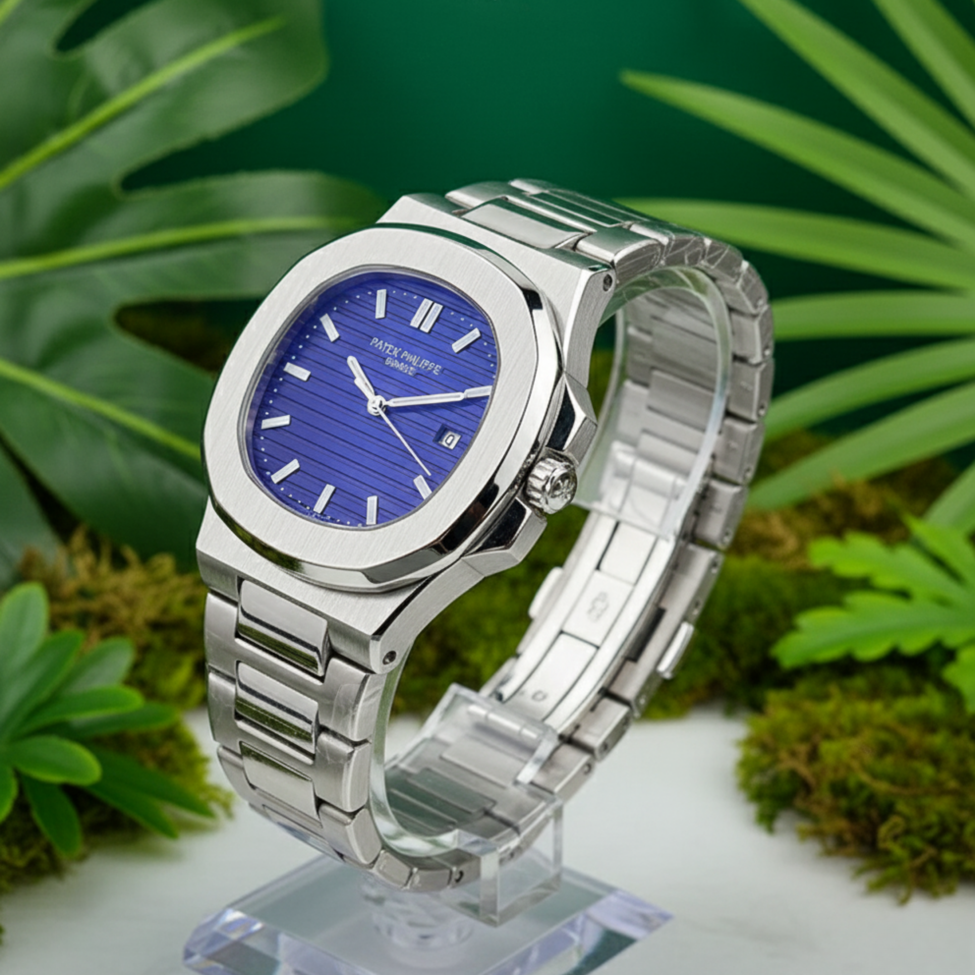 Silver watch with blue dial on a clear stand against a green leafy background